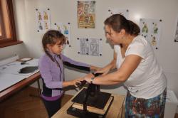 Účastnice edukačního programu si tiskne vlastní kartu na tiskařském lisu pod dozorem pedagoga. 