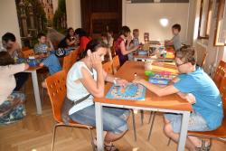 Malí i velcí návštěvníci hrají společenské stolní hry. 